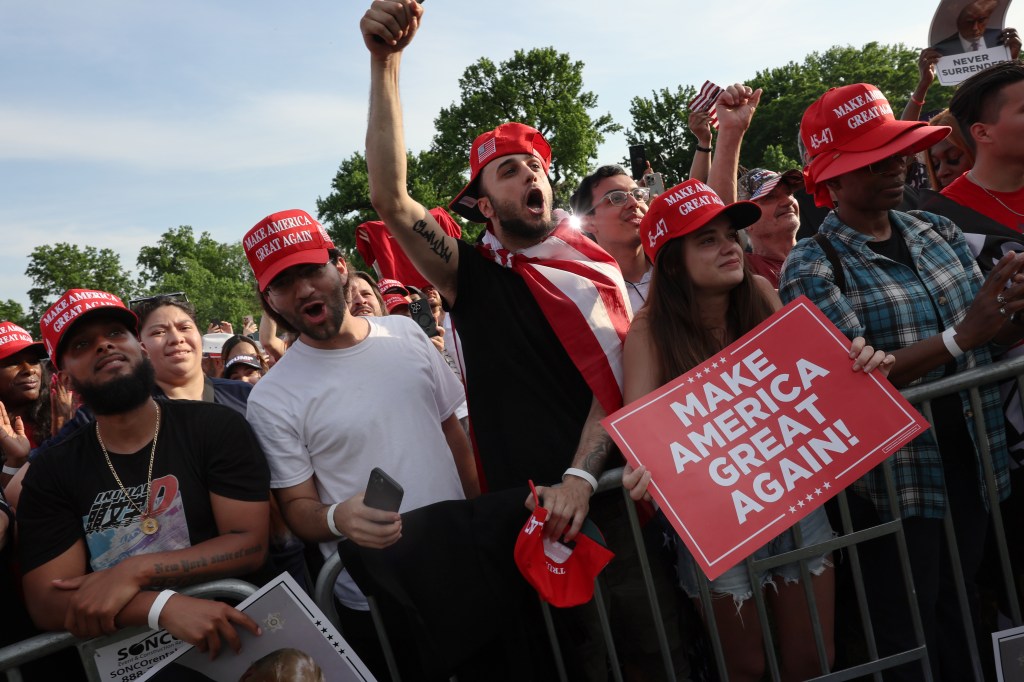 Trump supporters in red MAGA hats cheering in the front row at the rally.