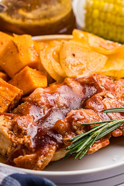 angled shot of bbq chicken and sweet potatoes on plate with rosemary