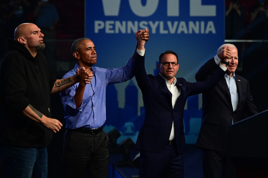 Democratic candidates John Fetterman and Josh Shapiro, along with former President Barack Obama and current President Joe Biden, raising their arms in unity at a rally in Philadelphia, Pennsylvania.