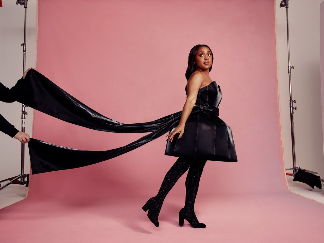 Quinta Brunson poses in a black dress before a pink seamless roll of paper.